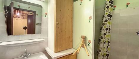 A bathroom with a sink, mirror, wooden door, and shower curtain with a floral pattern.