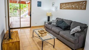 A living room with a grey sofa, a glass coffee table, a wooden TV stand, and a ceiling fan. - ★ Flat 1 - Modern 2 BR 2 Bath - 300m from beach ★ (Playas del Coco)