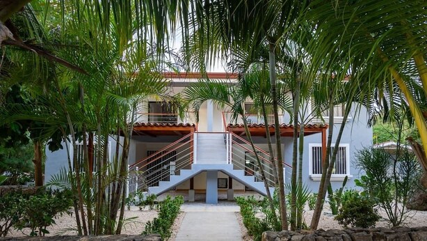 A modern building with a central staircase leading to a balcony, surrounded by lush greenery. - ★ Flat 1 - Modern 2 BR 2 Bath - 300m from beach ★ (Playas del Coco)