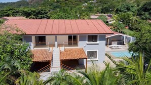 A modern house with a red-tiled roof, a swimming pool, and lush greenery surrounding it. - ★ Flat 1 - Modern 2 BR 2 Bath - 300m from beach ★ (Playas del Coco)
