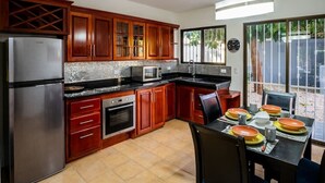A kitchen with wooden cabinets, a stainless steel refrigerator, a microwave, and a dining area with a table set for four. - ★ Flat 1 - Modern 2 BR 2 Bath - 300m from beach ★ (Playas del Coco)