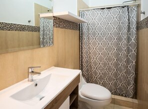 Een badkamer met een witte wastafel, toilet en een douchegordijn met een geometrisch patroon.