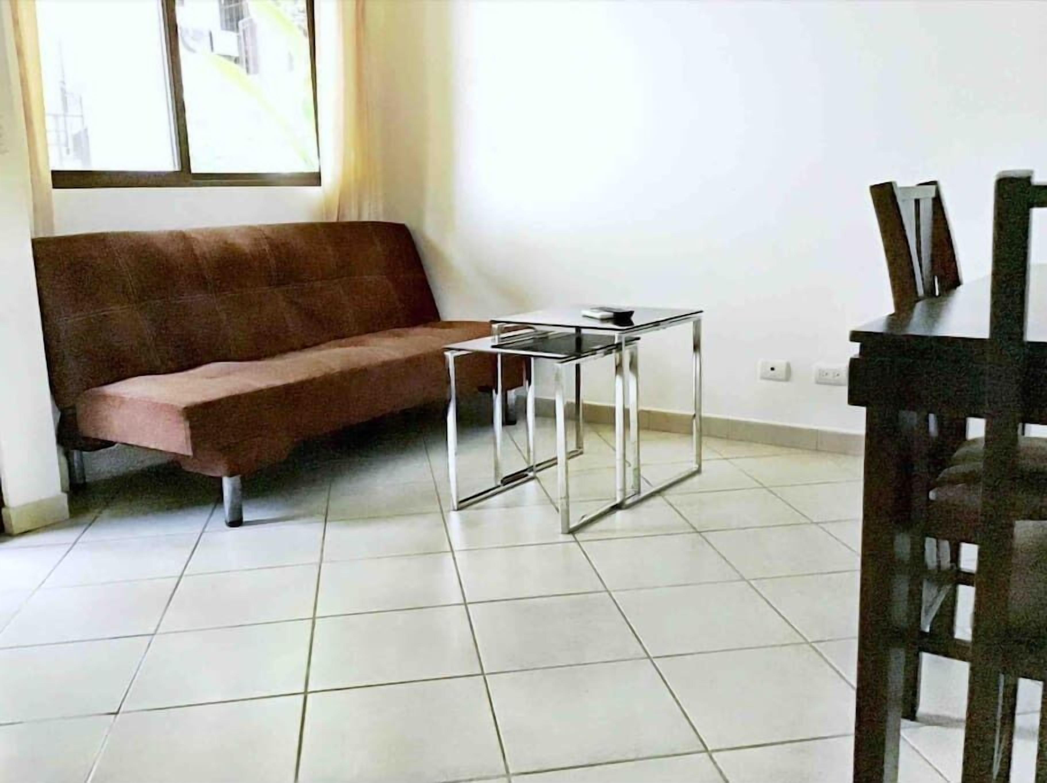 A room with a brown sofa, a small glass-top table, and a wooden chair.