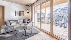 A modern living room with a sofa, coffee table, and large windows offering a mountain view. - Alpenstern Panoramalodgen (Damüls)
