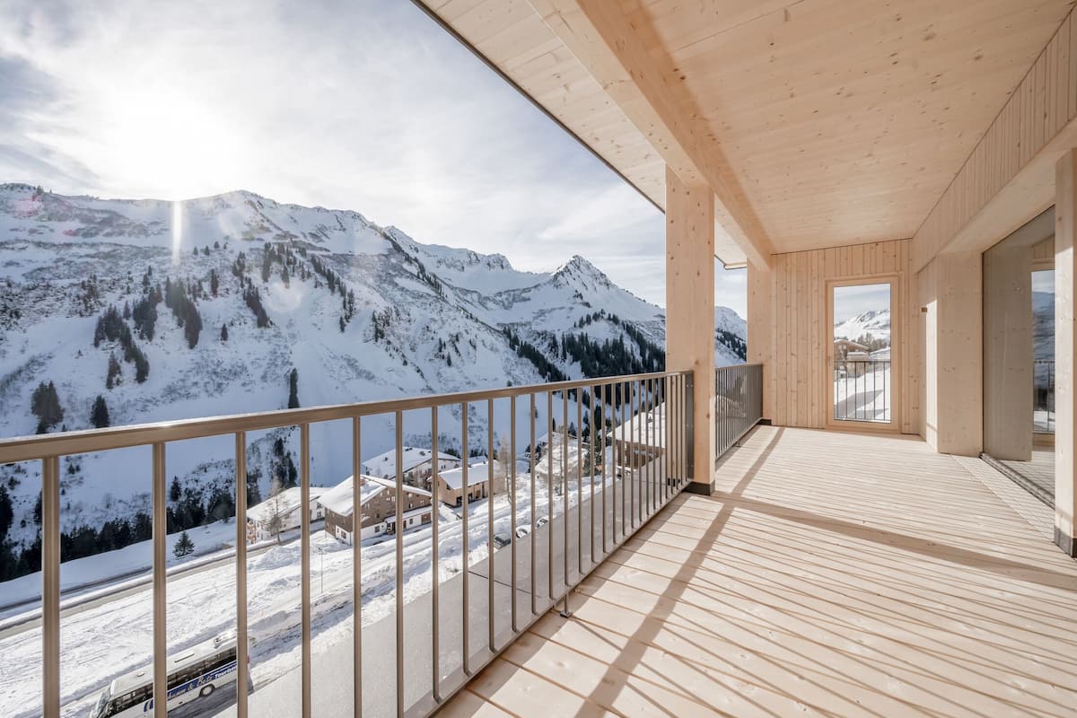 Een houten balkon met uitzicht op besneeuwde bergen en een heldere lucht.