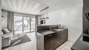 A modern kitchen with a central island, a dining area with a table and chairs, and a large sliding glass door leading to a balcony. - Alpenstern Panoramalodgen (Damüls)