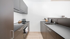 A modern kitchen with dark cabinetry, a black countertop, and a stainless steel range hood. - Alpenstern Panoramalodgen (Damüls)