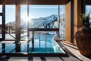 A modern indoor pool with a glass barrier, a view of a snowy mountain, and a large decorative plant. - Hotel Alpenstern (Damüls)