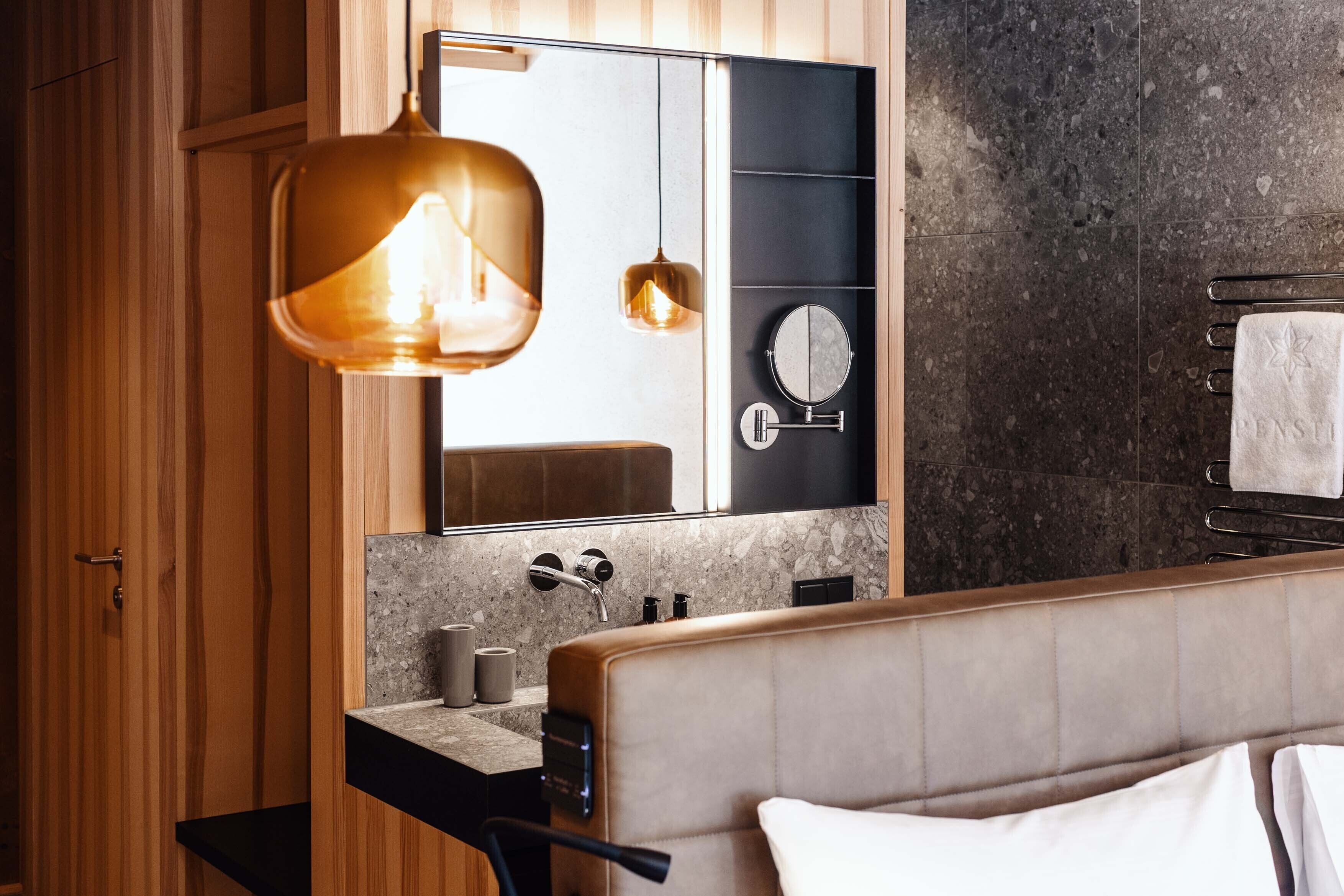Un baño moderno con tocador, un espejo grande, toallero y una lámpara colgante.