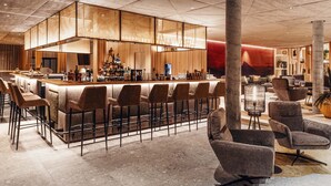 Un área de bar moderna con una barra alta, varios taburetes y una pantalla grande iluminada.