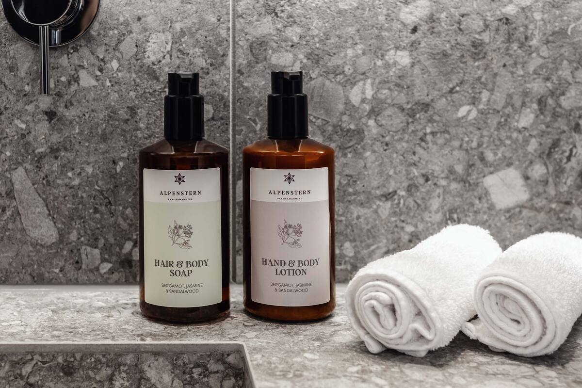 Two bottles of Alpenstern hair and body soap and lotion on a marble countertop with a rolled white towel beside them.