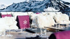 Una mesa de comedor con suaves almohadones de piel blanca, un mantel individual morado y copas de vino, con vistas a la montaña de fondo.