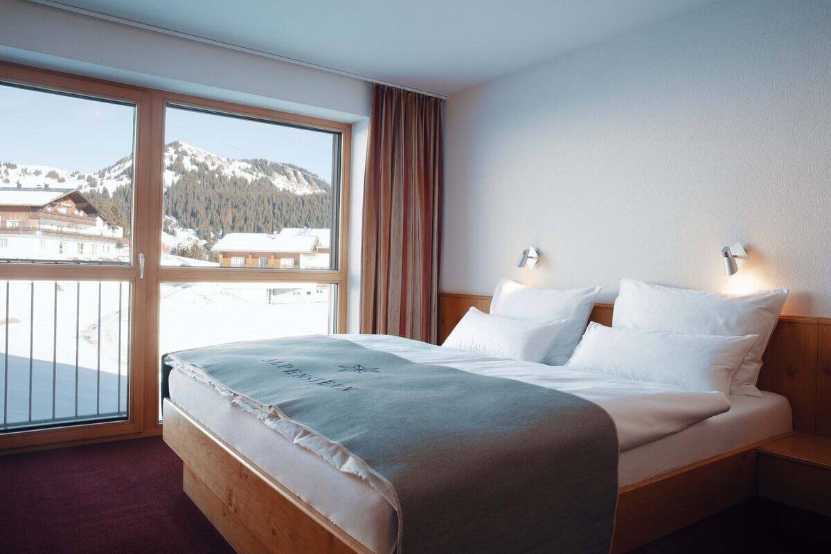 A hotel room with a large bed, two bedside tables, a window with a view of snow-covered mountains, and a curtain.