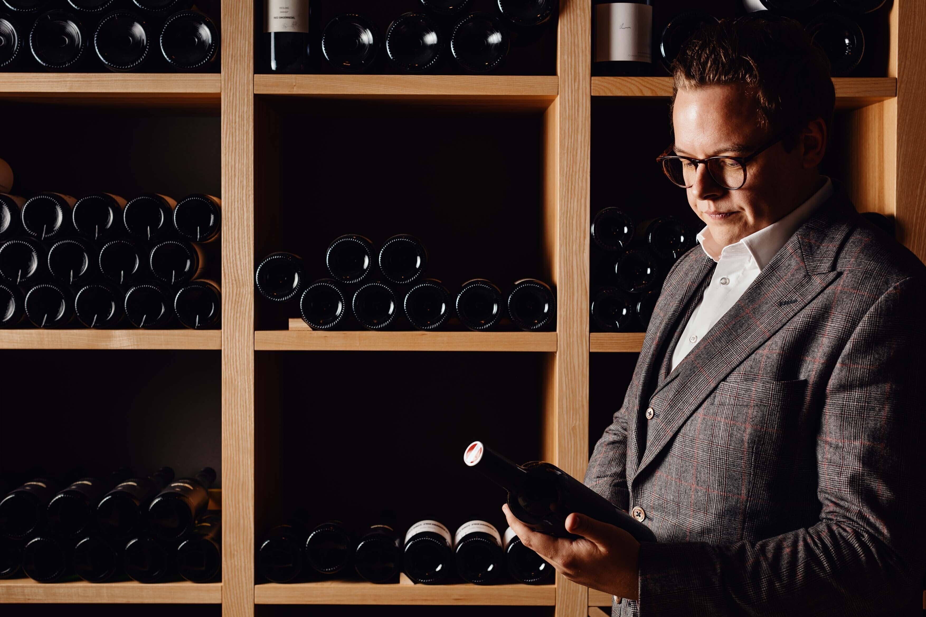A person holding a wine bottle in front of a wine rack filled with bottles.