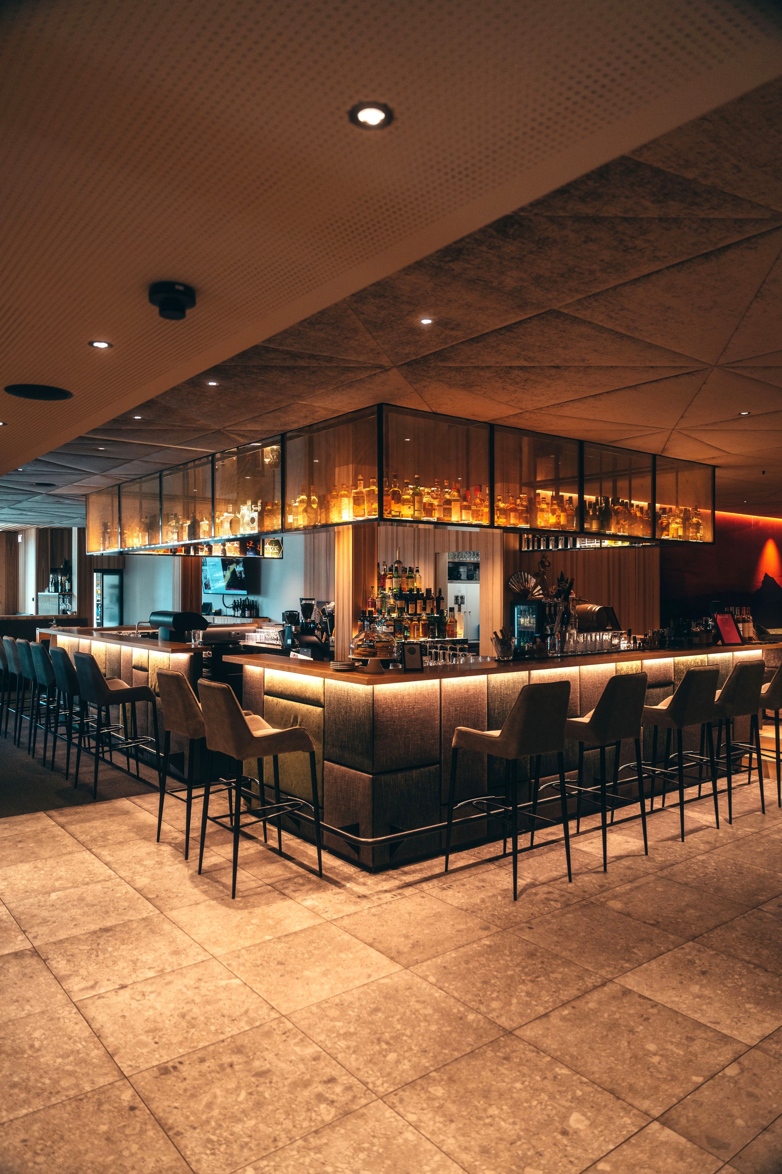 Eine Bar mit einer langen Theke, mehreren Hockern und einer Auswahl an Flaschen und Gläsern.