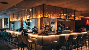 Eine Bar mit einer langen Theke, mehreren Hockern und einer Auswahl an Flaschen und Gläsern.
