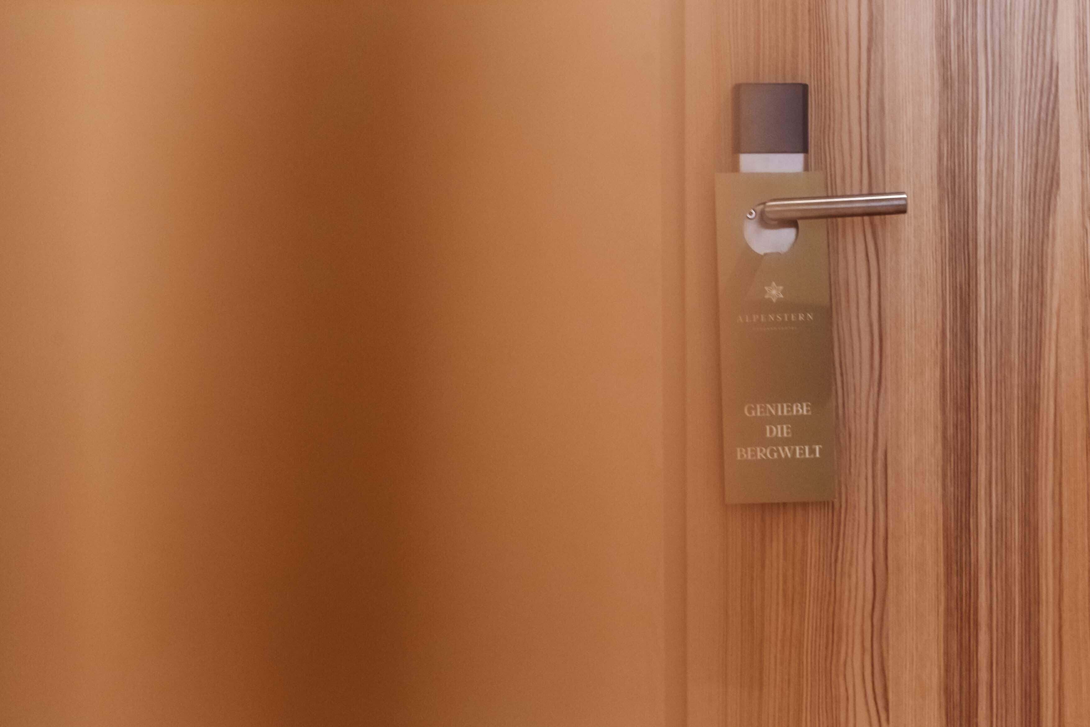 A wooden door with a metal handle and a card with the text "GENIEBE DIE BERGWELT" and "ALPFENSTERN".