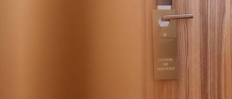 A wooden door with a metal handle and a card with the text "GENIEBE DIE BERGWELT" and "ALPFENSTERN".