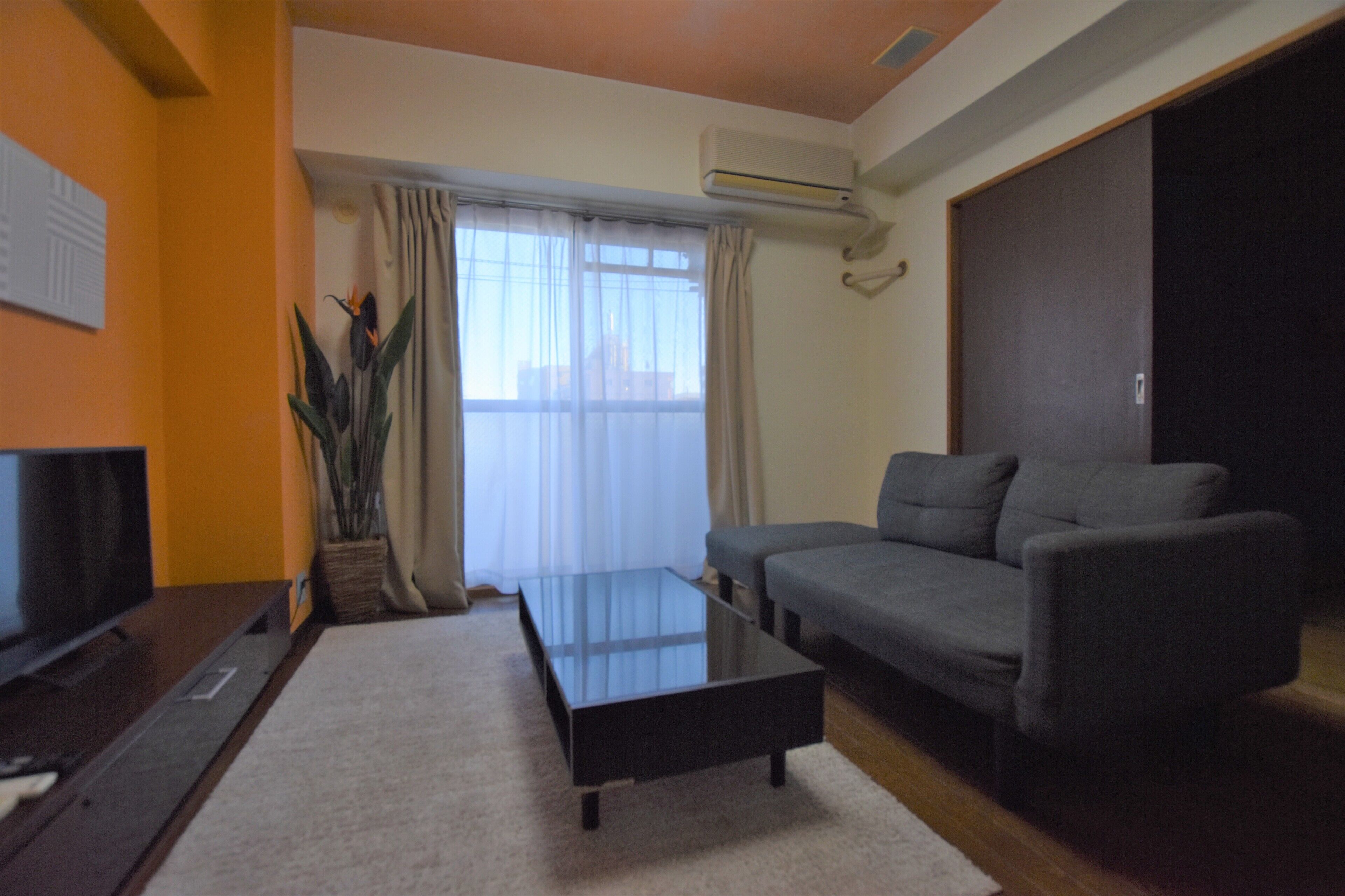 Una sala de estar con sofá, mesa de centro, televisor y ventana con cortinas.