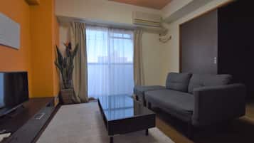 A living room with a sofa, a coffee table, a TV, and a window with curtains.