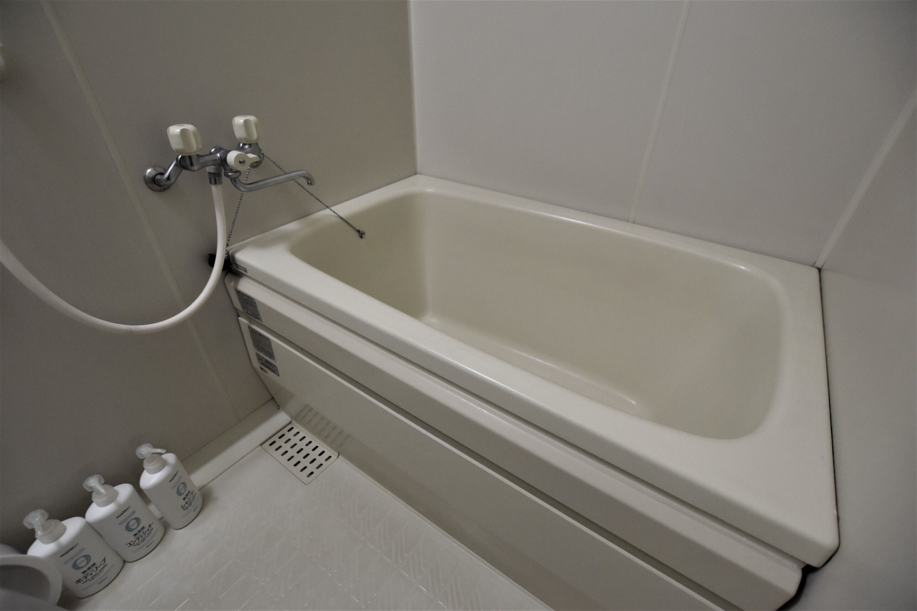 A bathroom with a bathtub, a shower, and a toilet. There are three bottles of hand soap on the floor.