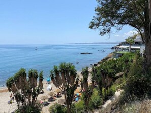 A coastal view with a beach, palm trees, and a large house overlooking the ocean. - Top floor apartment first line Golf Torrequebrada (Benalmádena)