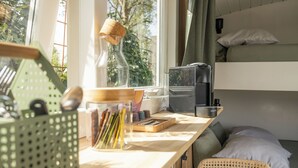 Una habitación pequeña con una cama litera, un escritorio modesto con varios objetos y una silla de mimbre.