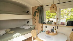 Habitación pequeña con una litera, una mesa de comedor y sillas, una lámpara colgante y una ventana con vistas a árboles.