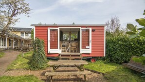 Una casa móvil roja con puertas abiertas, una mesa de picnic y un pequeño jardín.