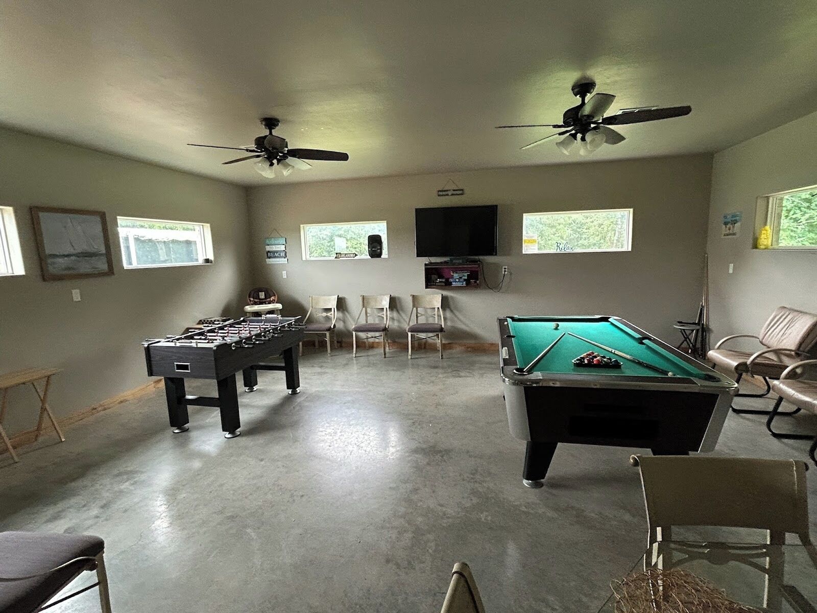 A recreational room with a pool table, foosball table, ceiling fans, and a television.