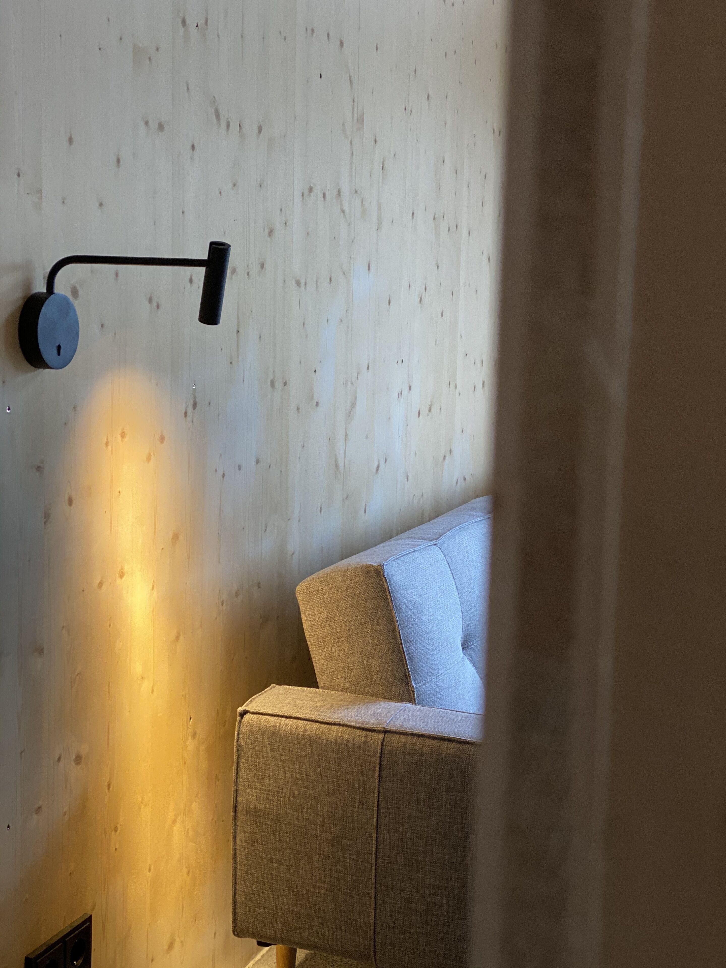 Ein modernes Zimmer mit einer Holzwand, einer Couch und einer wandmontierten Leuchte.