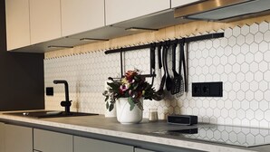 A modern kitchen with a white hexagonal tile backsplash, a stainless steel range hood, and a built-in dishwasher.