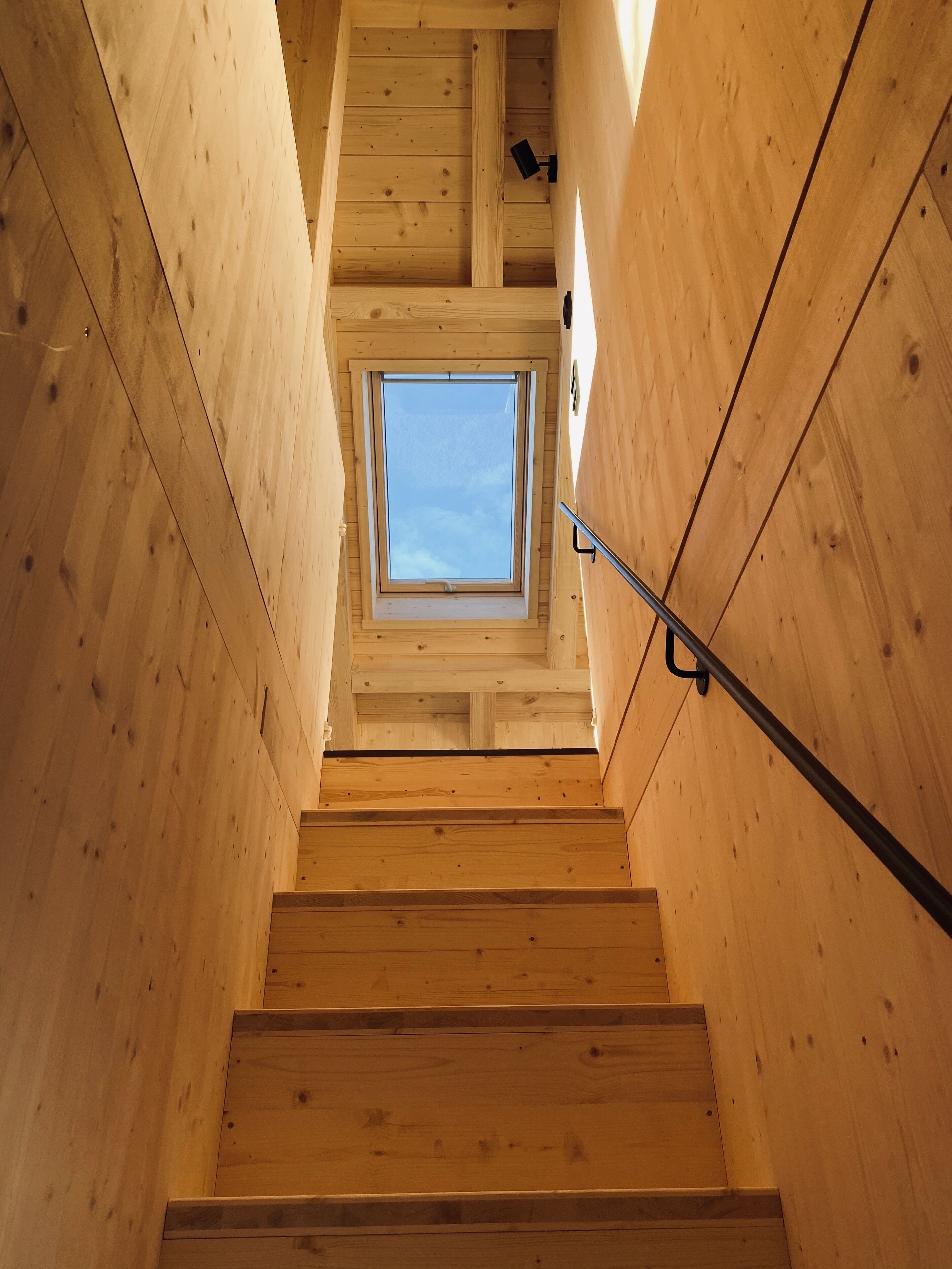 A wooden staircase with a skylight at the top.