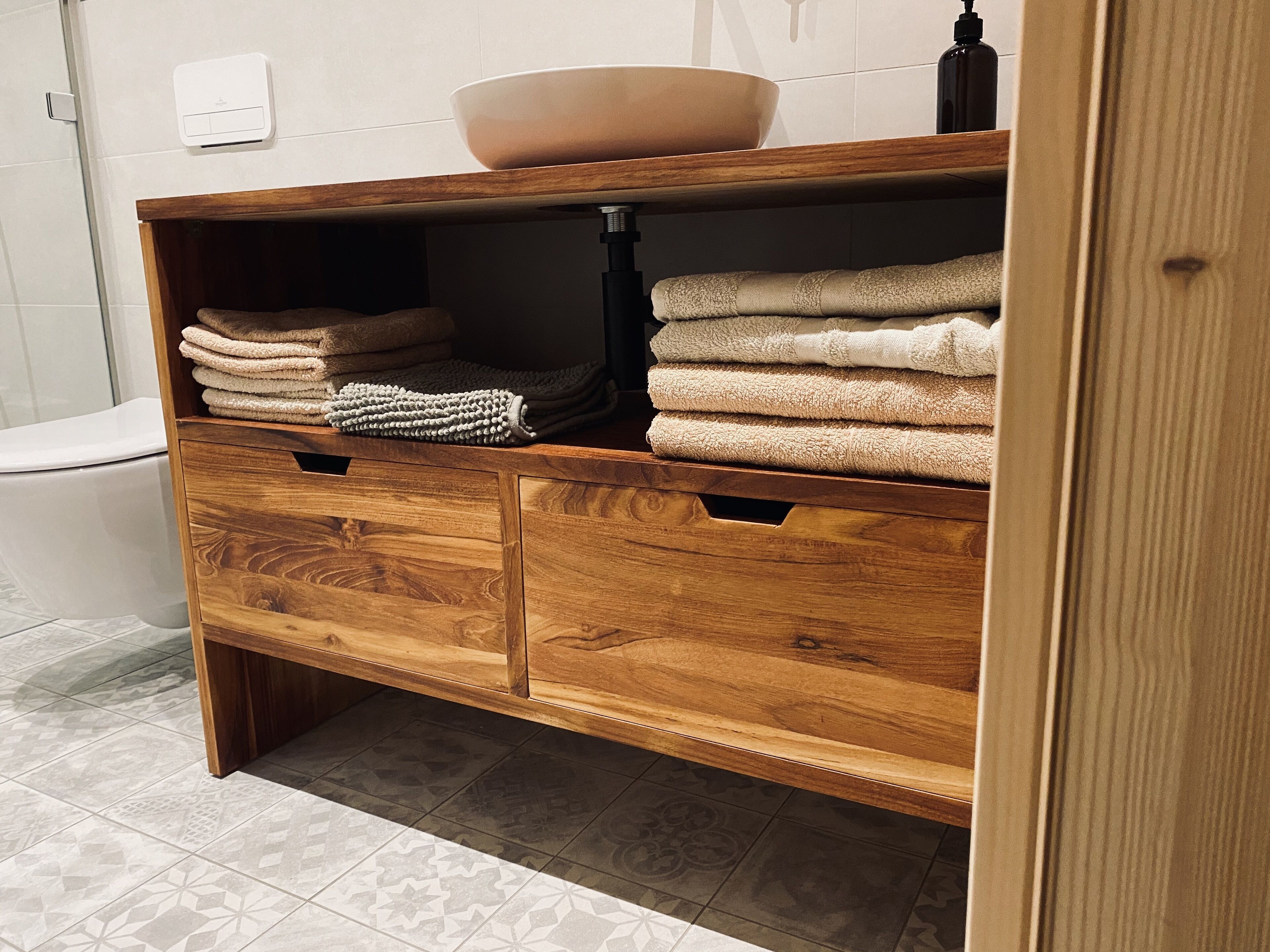 A wooden vanity with a bowl sink, stacked towels, and a soap dispenser.