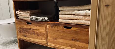 A wooden vanity with a bowl sink, stacked towels, and a soap dispenser.