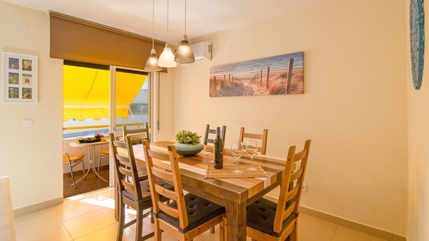 Un comedor con una mesa de madera, sillas, una planta y un cuadro en la pared.