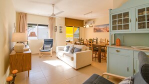 Una sala de estar con sofá, una mesa de comedor, sillas, un ventilador de techo y una zona de cocina con armarios.