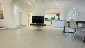 Un vaste espace de vie comprenant un téléviseur à écran plat, une table à manger avec des chaises, et une cuisine située à l’arrière-plan.