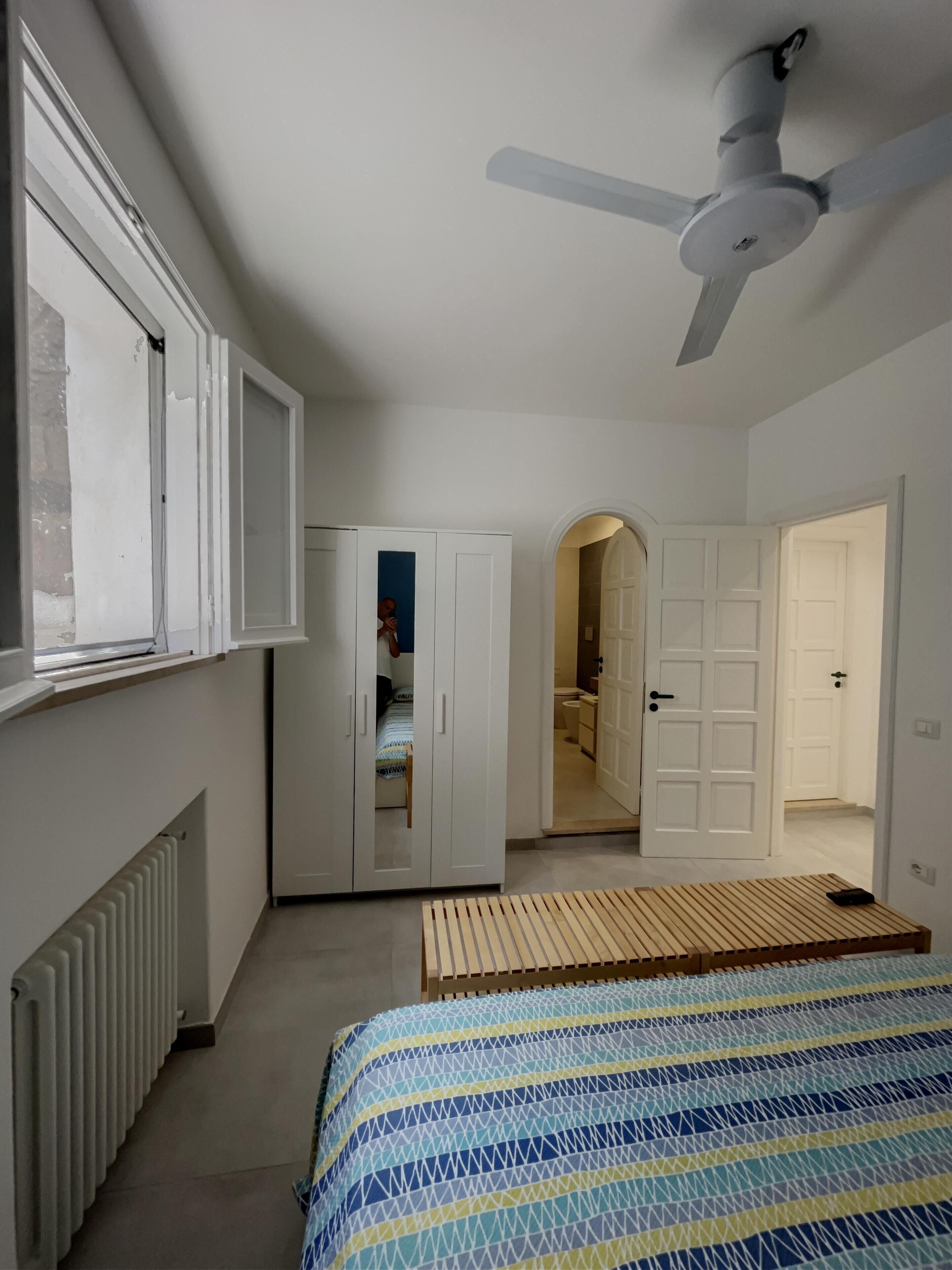 Ein Schlafzimmer mit Bett, Deckenventilator, Kleiderschrank und einem durchgegangenen Tür zugehörigen Badezimmer.