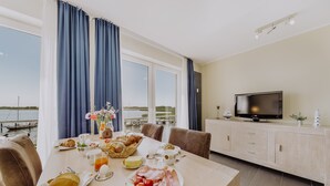 Un comedor con una mesa dispuesta para el desayuno, un televisor en un mueble y vista al agua.