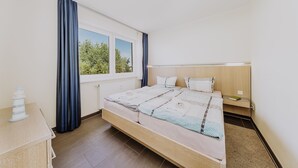 Un dormitorio con una cama grande, una mesita de noche, cortinas en la ventana y vistas a árboles fuera.