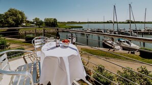 Un balcón con una mesa preparada para dos personas, con vista a un puerto deportivo y barcos.