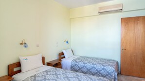 Une chambre avec deux lits, des têtes de lit en bois, une porte en bois et un appareil de climatisation fixé au mur.