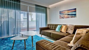 Een moderne woonkamer met een bank, een bijzettafeltje en een groot raam met gordijnen.