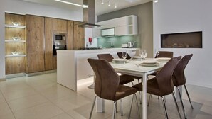Een moderne keuken met een centraal eiland, inbouwapparatuur en een eethoek met bruine stoelen.