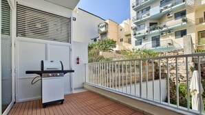 Een balkon met een barbecue, een witte deur en een stenen muur.