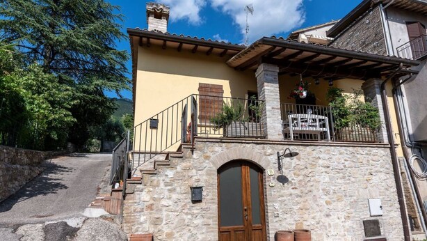 Un edificio de piedra con una puerta de madera, un balcón con barandilla y una pequeña escalera que lleva a la entrada.