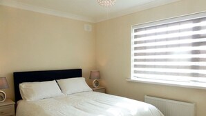 A bedroom with a bed, two bedside tables, a window with blinds, and a radiator. - Bolams Holiday Home (Thomastown)