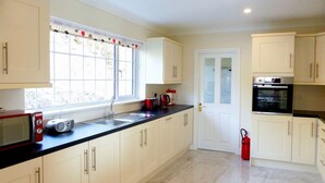A modern kitchen with white cabinets, a black countertop, a microwave, a coffee maker, and a red fire extinguisher. - Bolams Holiday Home (Thomastown)