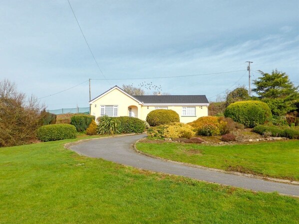 A single-story house with a curved driveway, surrounded by well-maintained lawns and hedges. - Bolams Holiday Home (Thomastown)